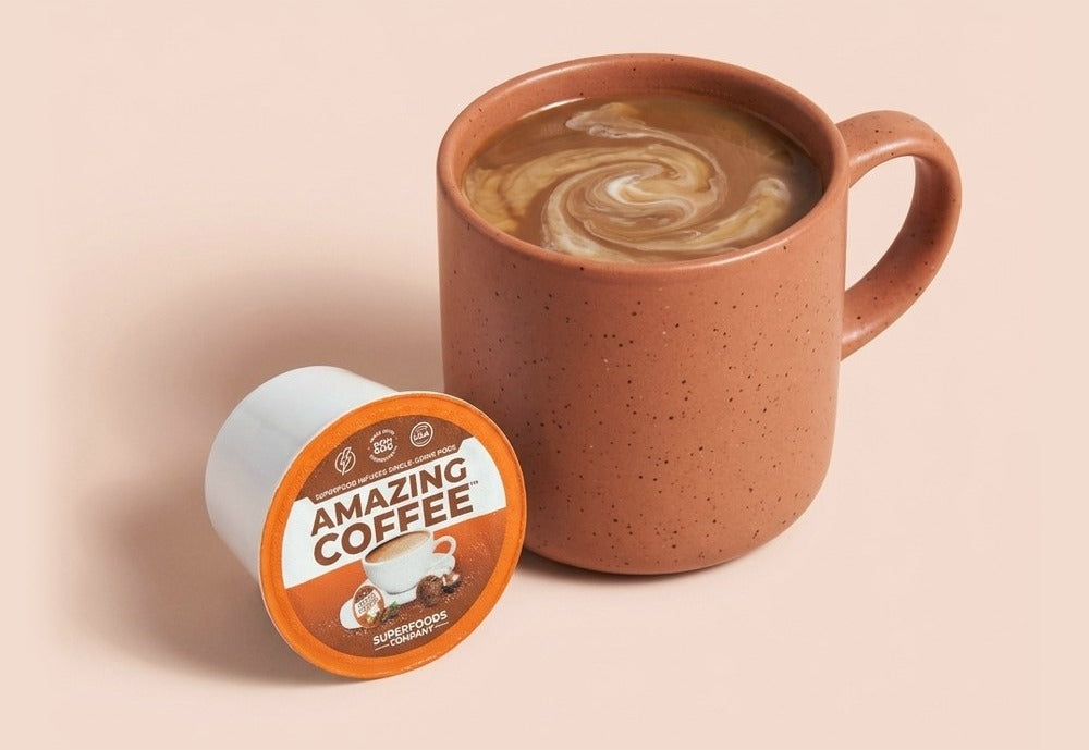 A mug of cocoa-flavored Amazing Coffee with cream swirled through it, beside a single-serve pod