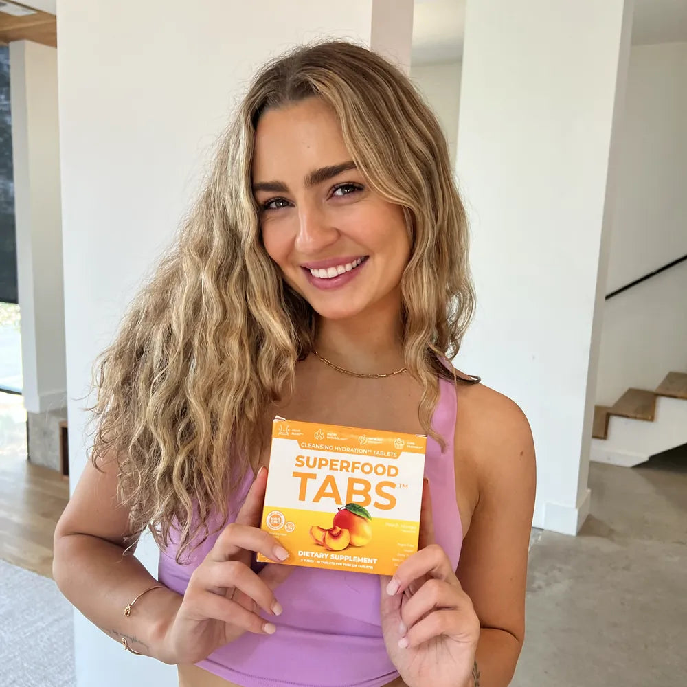 A smiling woman holding a carton of Superfood Tabs Peach Mango